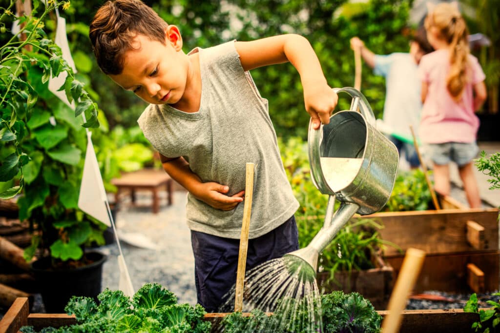 Child holding watering can helping water the garden