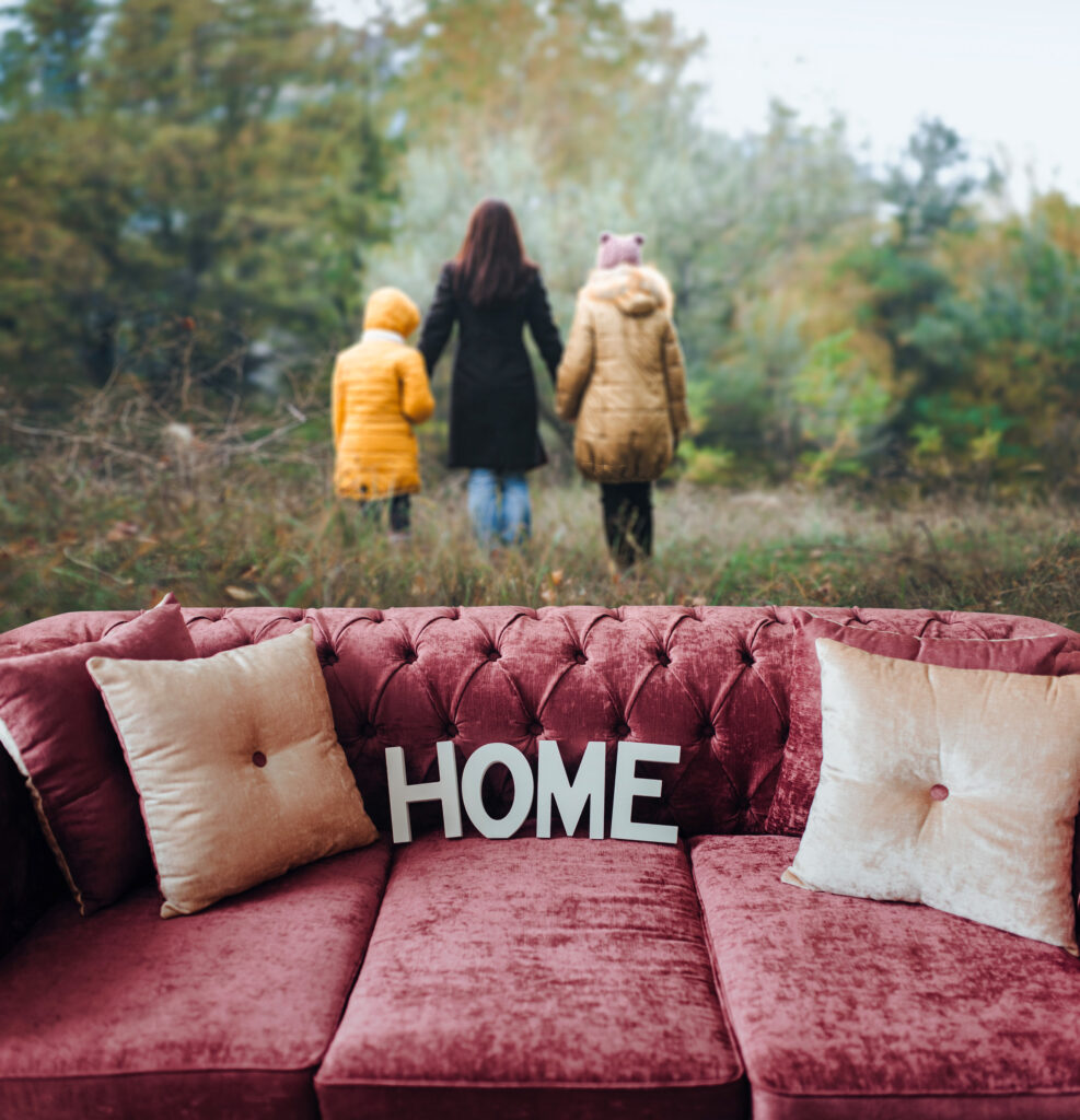 A sad picture showing a couch with a pillow that says home with the family leaving it in the distance