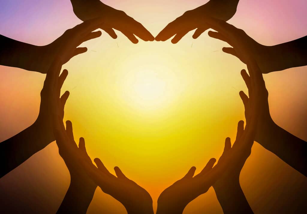 Multiple hands form an outline of a heart to communicate Community involvement. Against the background of the sun.