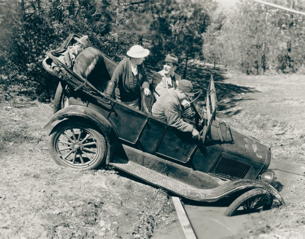 Funny vintage car stuck in a ditch. Man driving. Woman in the back in discussion with the driver.